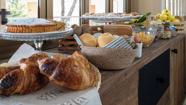 A buffet with various baked goods, including pastries and bread, arranged on a wooden counter. - hotel ristorante Donatella (Posada)