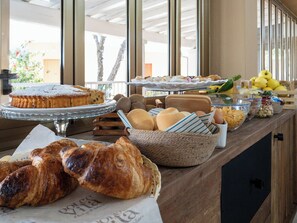 A buffet with various baked goods, including pastries and bread, arranged on a wooden counter. - hotel ristorante Donatella (Posada)