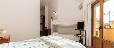 A bedroom with a bunk bed, a desk, a chair, a TV on a stand, and a window with a view of buildings.