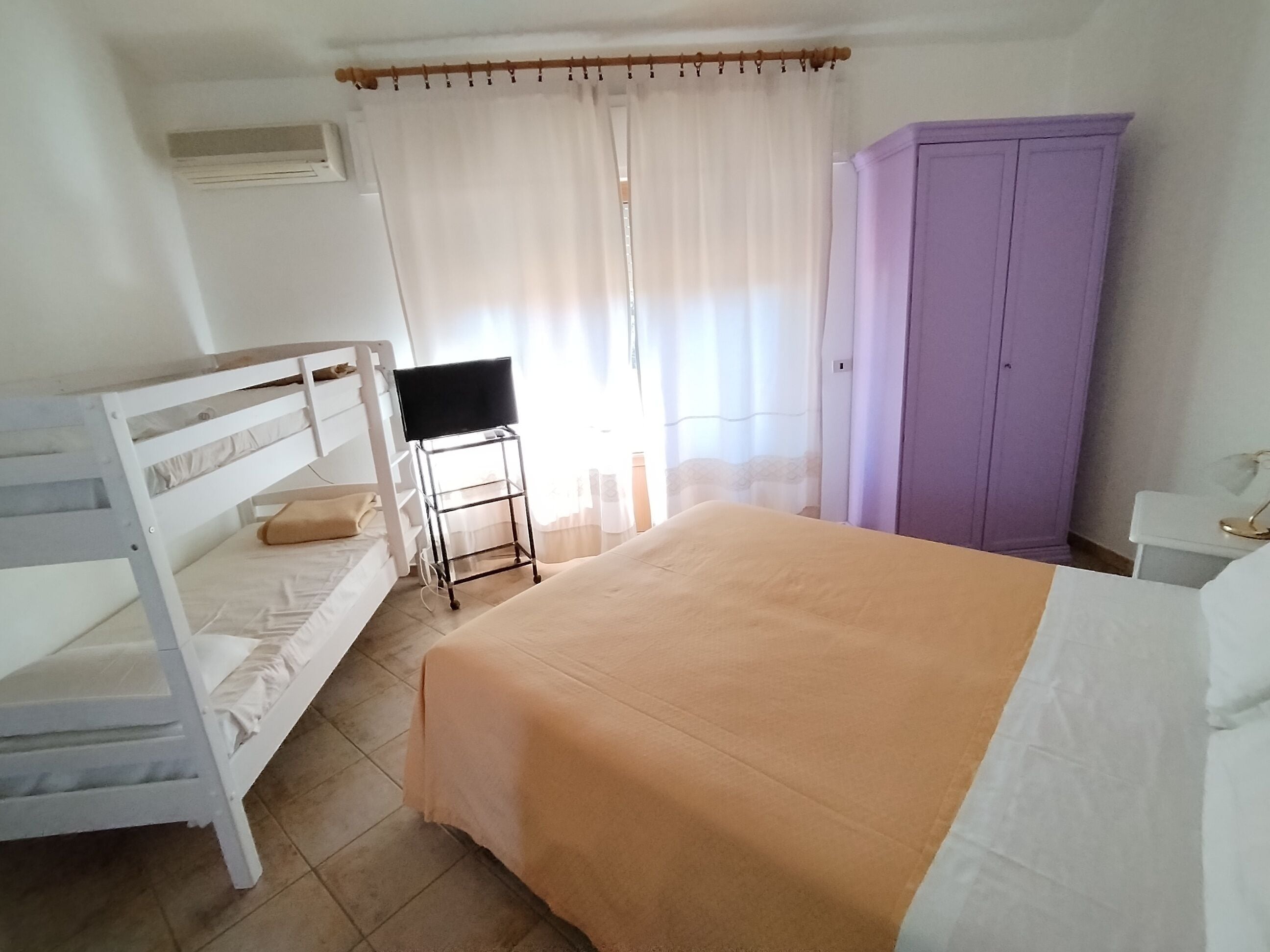 Un dormitorio con una cama individual, una litera, un armario y un televisor sobre un mueble.