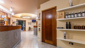 A hotel reception area with a wooden reception desk, a wall-mounted TV, and shelves with bottles. - hotel ristorante Donatella (Posada)