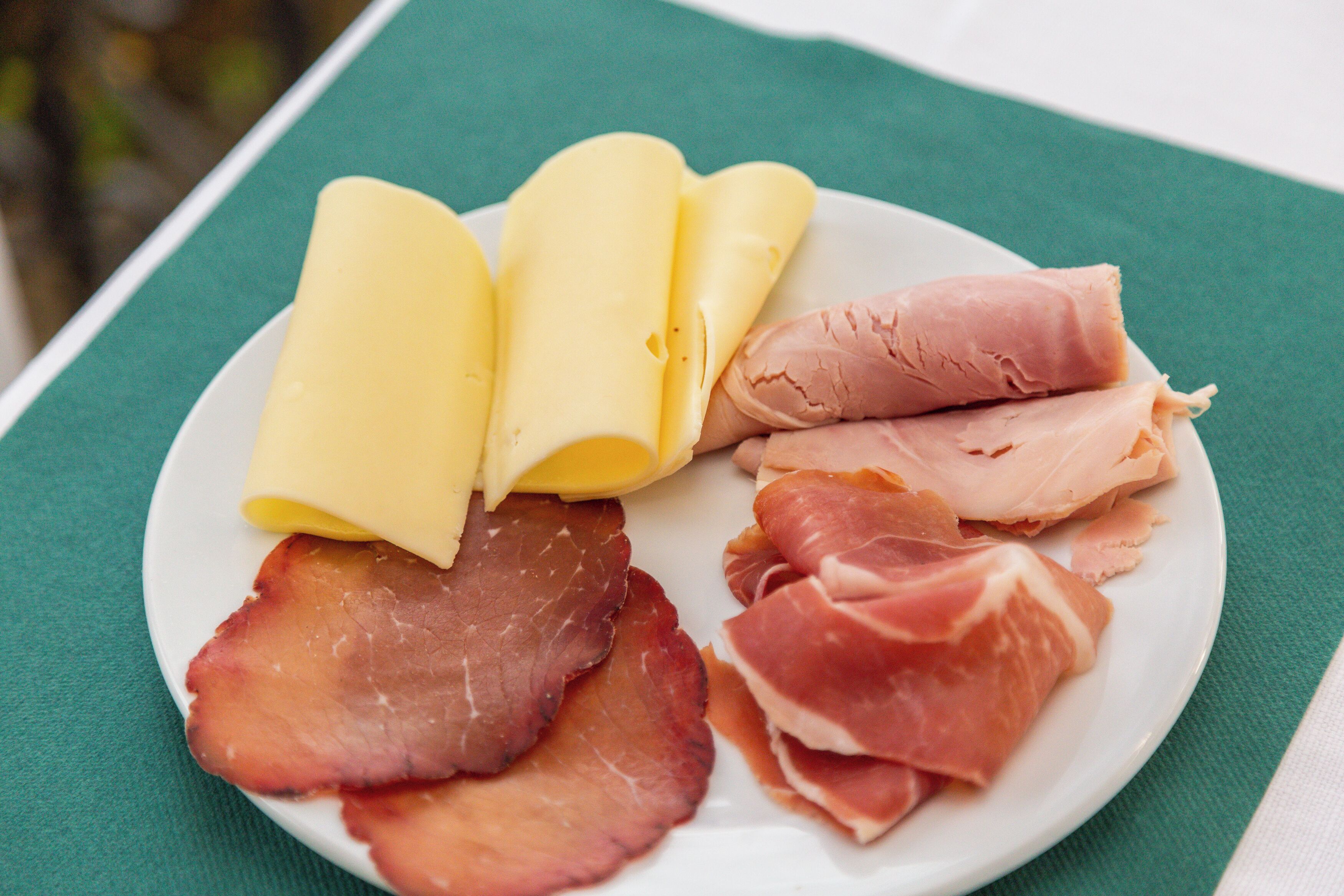 A plate with slices of ham and cheese on a green tablecloth.