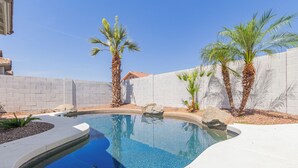Une piscine à bordures incurvées, entourée d’un mur blanc et de palmiers.