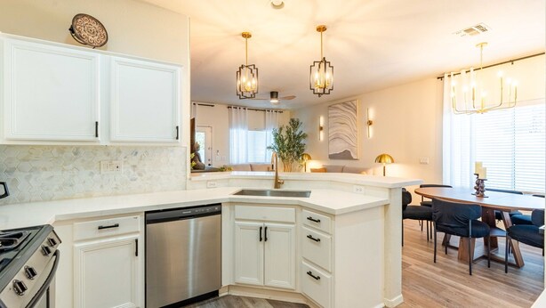 Une cuisine moderne avec des meubles blancs, un lave-vaisselle, une cuisinière et un coin repas comprenant une table et des chaises.