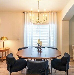 A dining area with a round table, six chairs, a chandelier, and a window with blinds. - Budget friendly monthly rental 4-bedroom house in serene Gilbert with large pool (Gilbert)