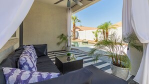 Une terrasse ensoleillée avec un canapé noir, une petite table et un ventilateur de plafond.