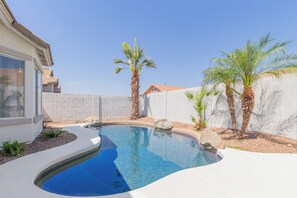 A swimming pool with a curved edge, surrounded by a white wall and palm trees. - Budget friendly monthly rental 4-bedroom house in serene Gilbert with large pool (Gilbert)