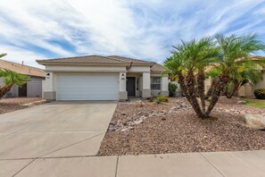 A single-story house with a white garage door, a front porch, and a small garden with palm trees and rocks. - Budget friendly monthly rental 4-bedroom house in serene Gilbert with large pool (Gilbert)