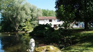A house with a tiled roof, surrounded by greenery and a pond. - Gîte des roties: Restored Family Home with Pool in a 7-Hectare Park (Poncins)