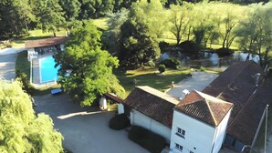 A residential area with a swimming pool, a white building with a red roof, and surrounding greenery. - Gîte des roties: Restored Family Home with Pool in a 7-Hectare Park (Poncins)