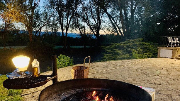 A fire pit with burning coals, a bottle, and a basket on a stone patio. - Gîte des roties: Restored Family Home with Pool in a 7-Hectare Park (Poncins)