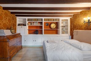 Un dormitorio con una estantería empotrada, un aparador de madera y una cama con ropa blanca.