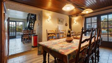 A dining area with a wooden table and chairs, a patterned tablecloth, and a view through a window.