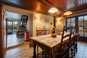 A dining area with a wooden table and chairs, a patterned tablecloth, and a view through a window. - Gîte des roties: Restored Family Home with Pool in a 7-Hectare Park (Poncins)