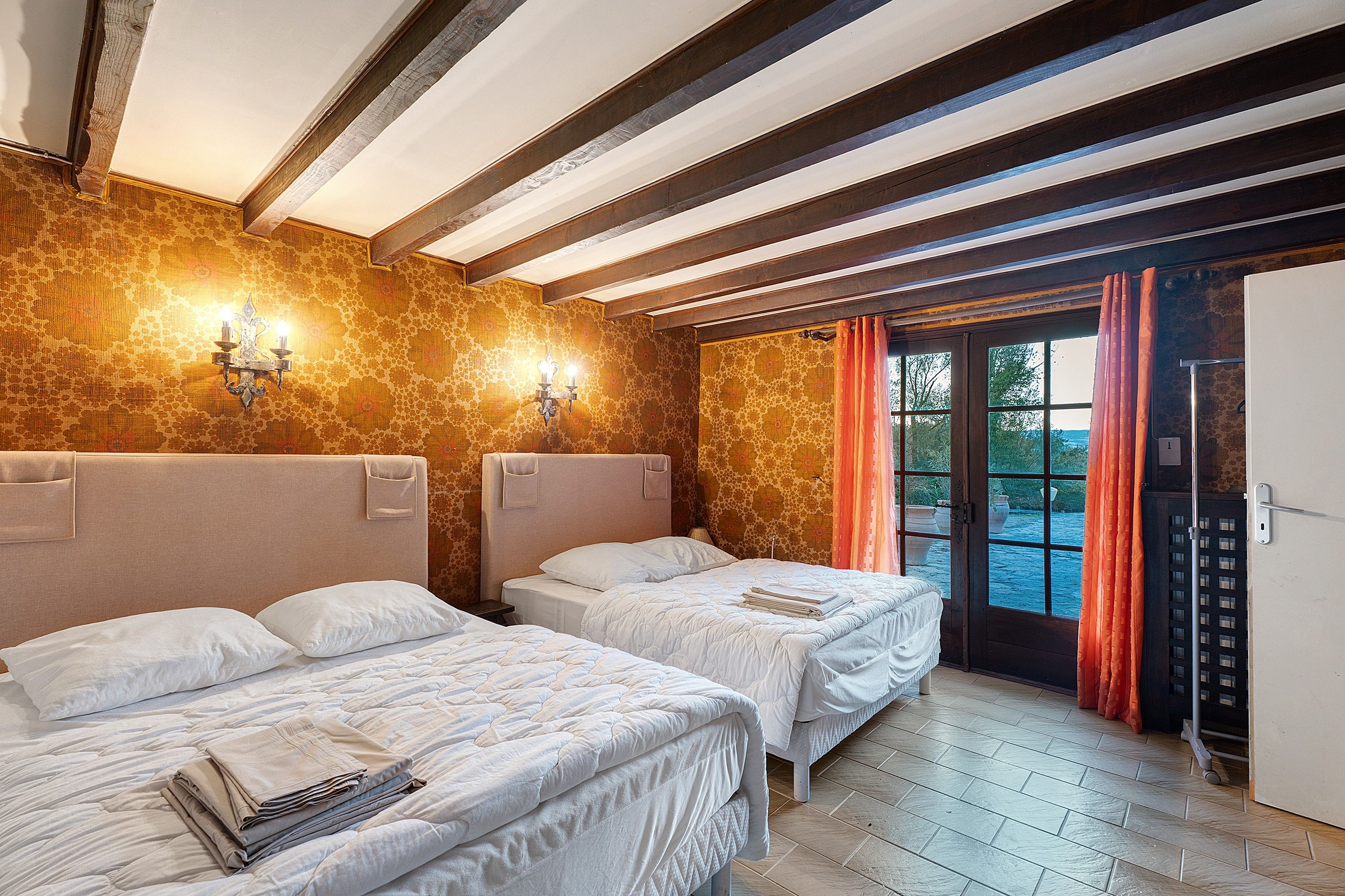 Una habitación con dos camas, techo de madera, pared con diseño y una puerta que da al exterior.