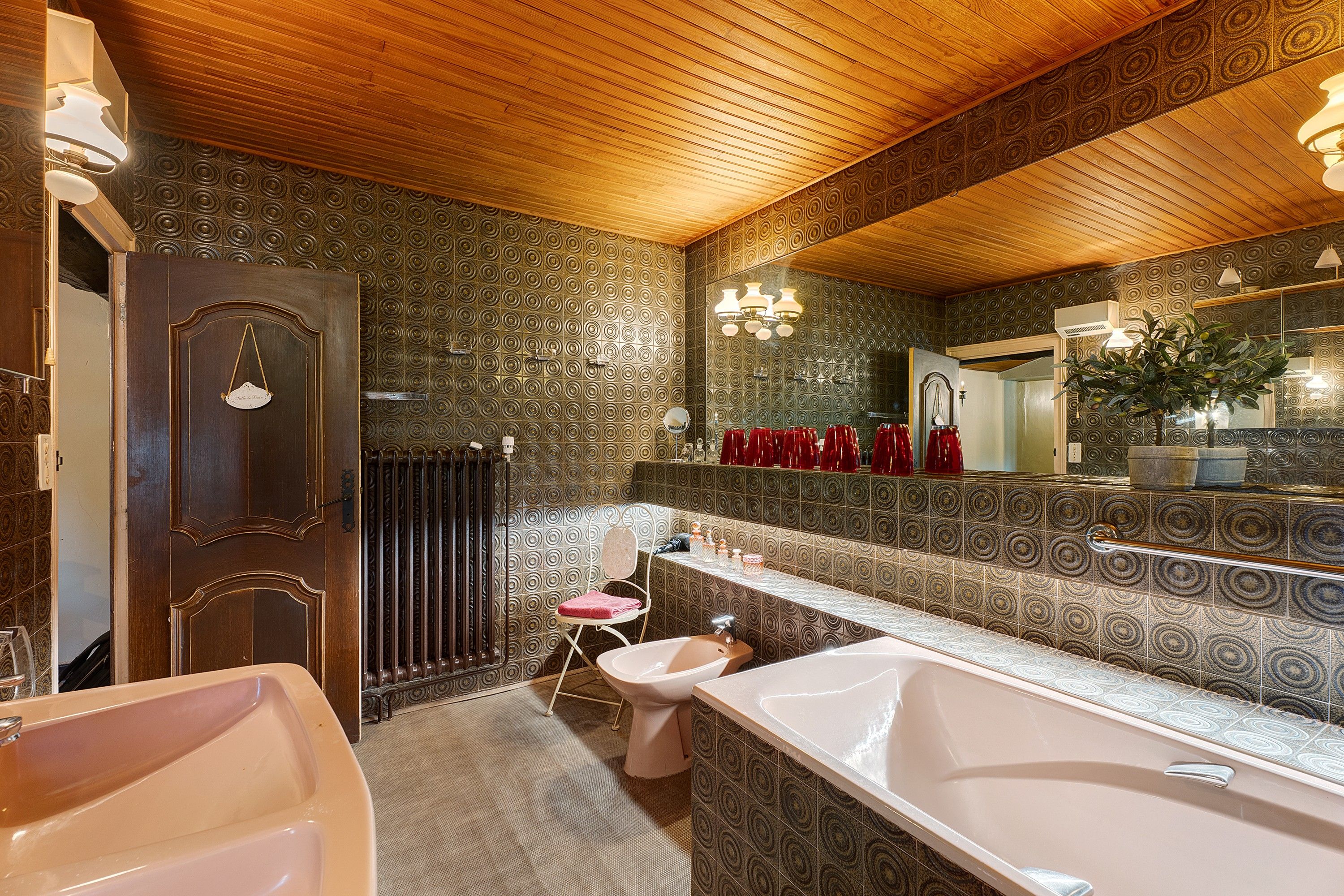 Une salle de bain avec un plafond en bois, un grand miroir, une baignoire, des toilettes et un lavabo.