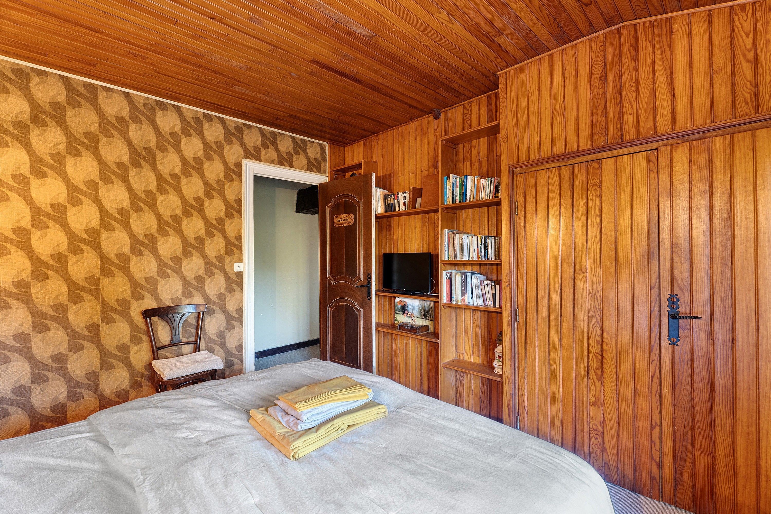 A room with a bed, wooden wardrobe, and bookshelves.