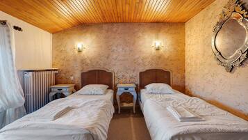Habitación de hotel con dos camas individuales, techo de madera, papel tapiz floral, un espejo y un radiador.
