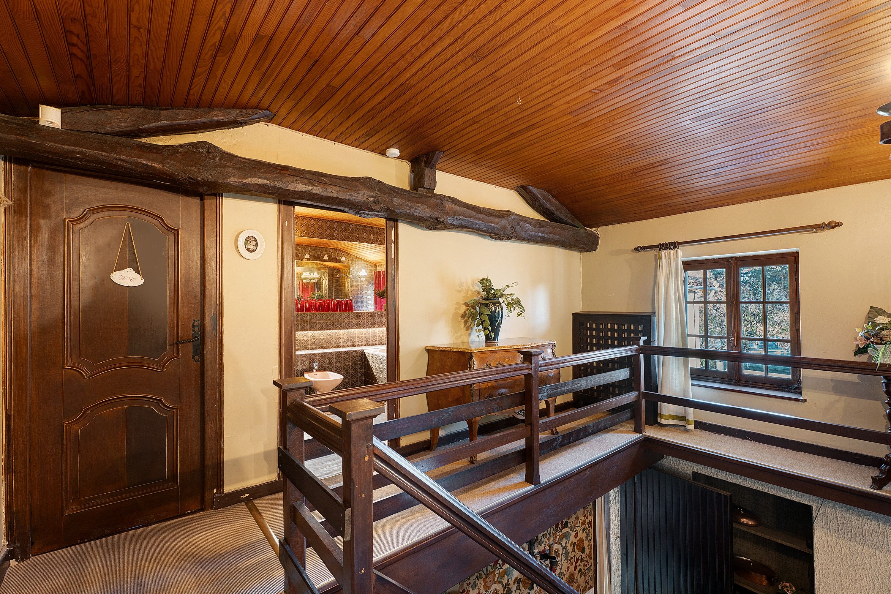 Una scala in legno con ringhiera che conduce a una stanza con soffitto in legno e una finestra.