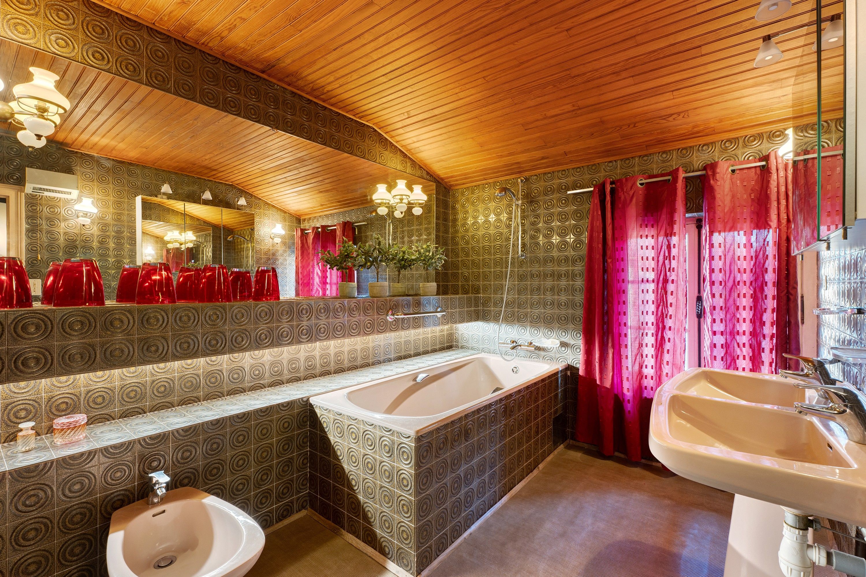 A bathroom with a wooden ceiling, a large mirror, two sinks, a bathtub, and patterned walls.