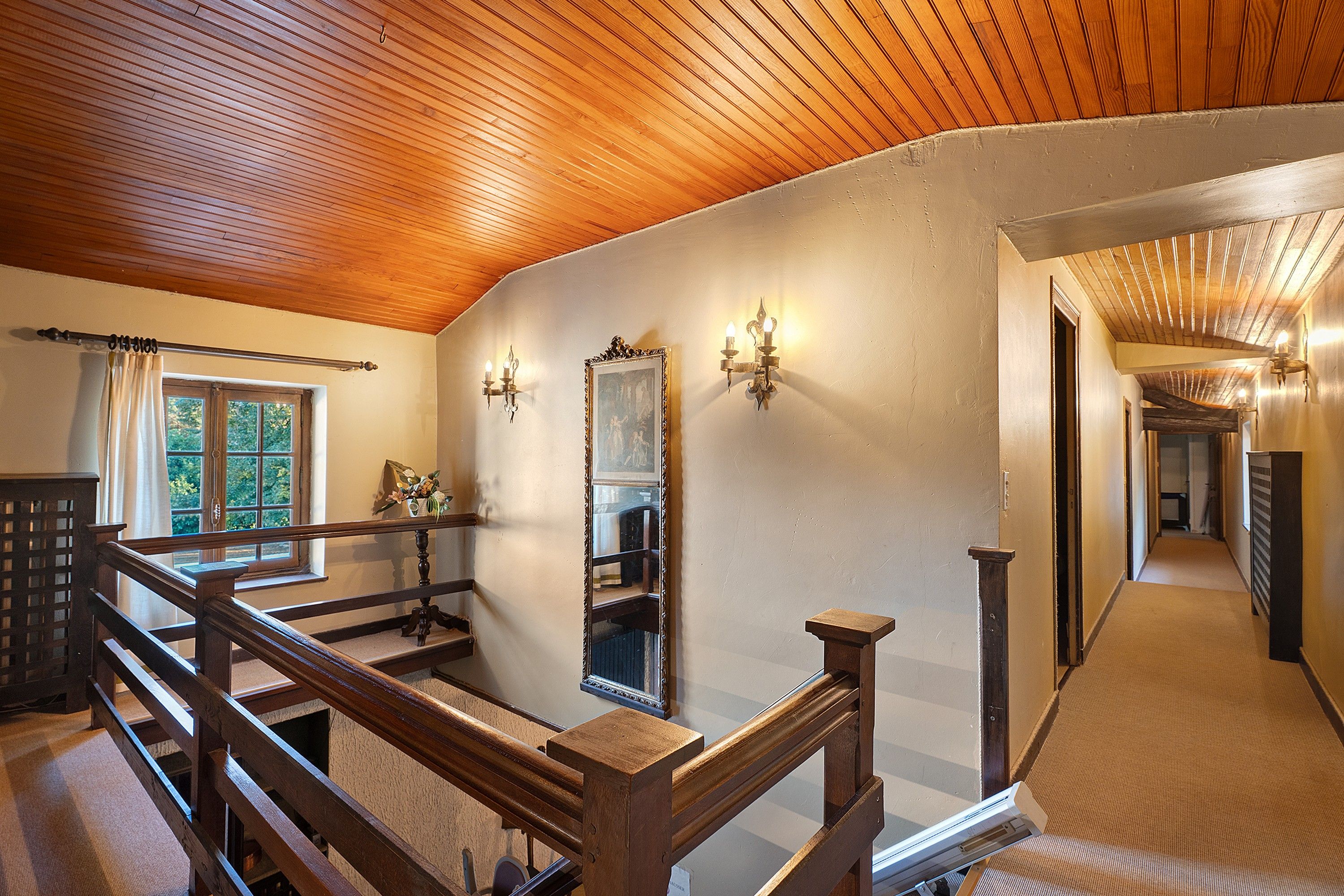 Un escalier en bois avec une rampe, un miroir fixé au mur et un luminaire.