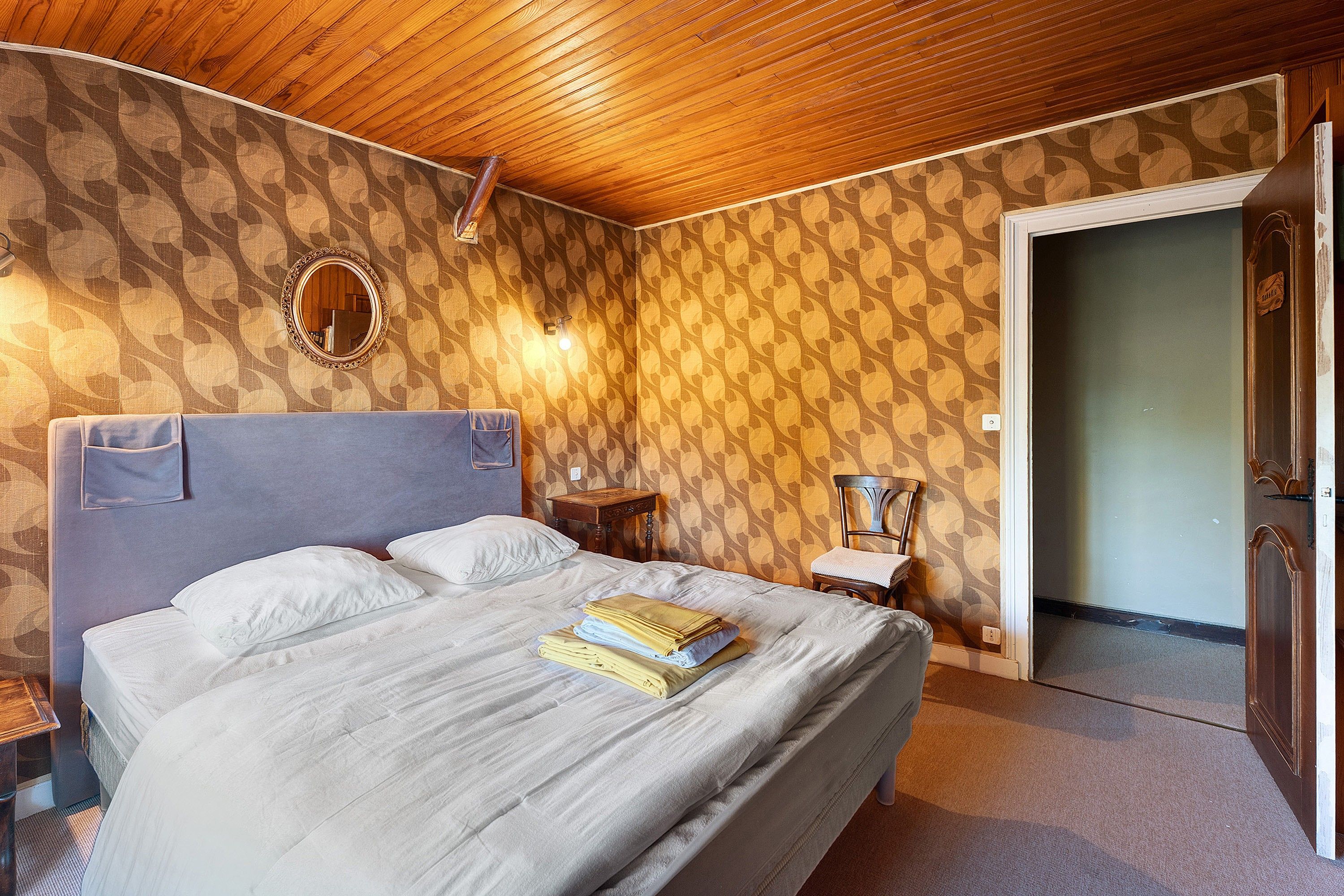 A hotel room with a large bed, a wooden ceiling, a mirror, and a door leading to another room.