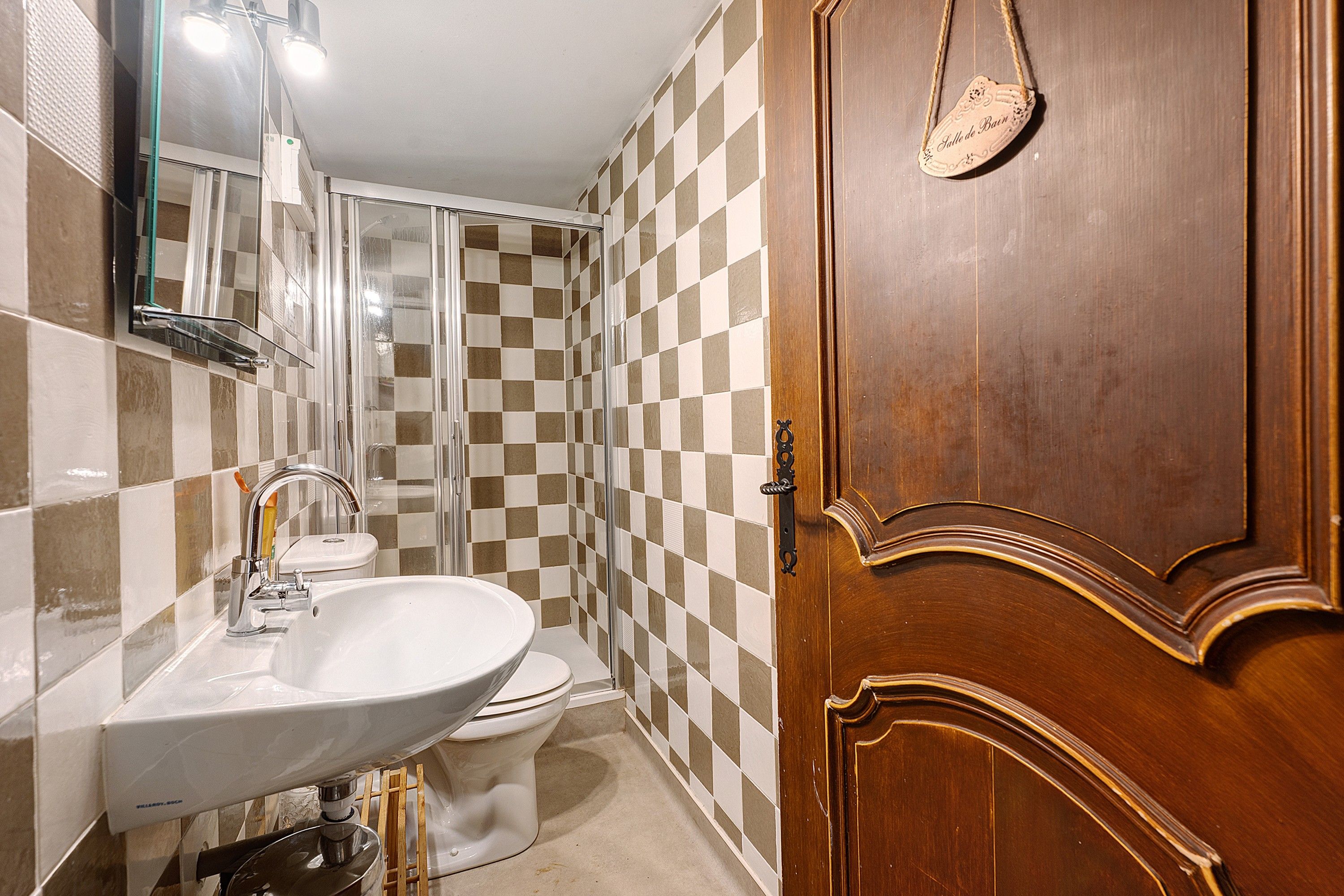 Une salle de bain avec un mur recouvert de carreaux à motifs, une porte en bois, un lavabo blanc et des toilettes.