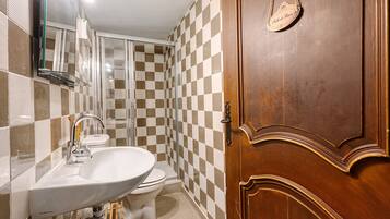 Une salle de bain avec un mur recouvert de carreaux à motifs, une porte en bois, un lavabo blanc et des toilettes.