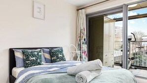 A bedroom with a bed, pillows, a rolled towel, a window, and a door leading to an outdoor area. - *Modern Spacious 1 Bedroom Flat in Camden* (London)