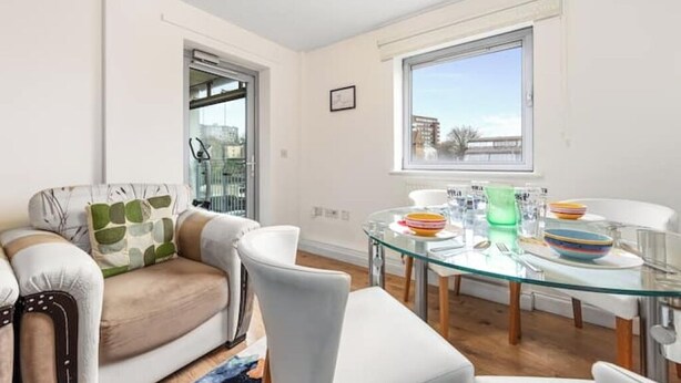 A modern living room with a glass dining table, white sofas, and a large window providing a view of the city. - *Modern Spacious 1 Bedroom Flat in Camden* (London)