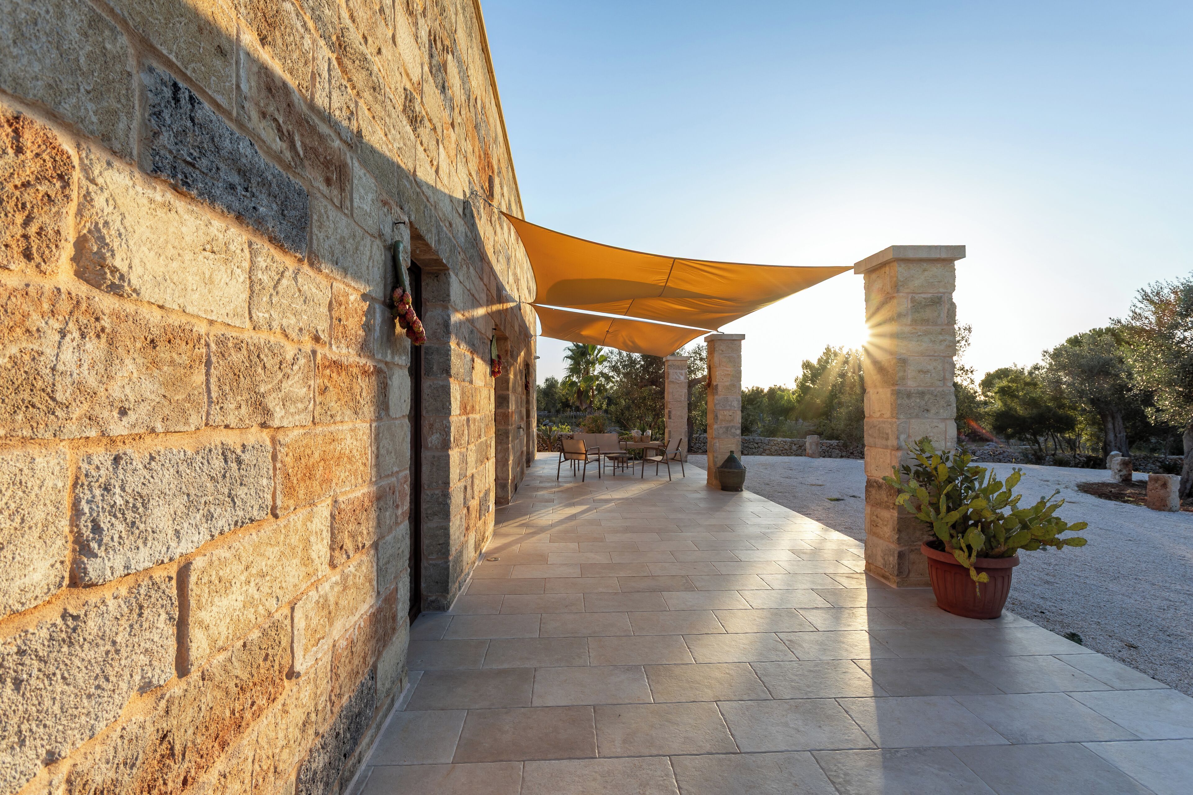 A stone building with a patio area featuring a table and chairs, a potted plant, and a yellow canopy providing shade.
