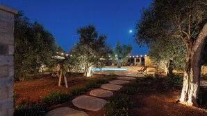 A nighttime outdoor area with a stone pathway leading to a pool, surrounded by trees and illuminated by string lights. - Exclusive villa with pool among aromas, colors and centuries-old olive trees of Salento (Spongano)