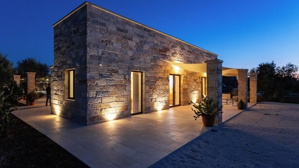 A modern stone building with a covered patio area, large windows, and potted plants. - Exclusive villa with pool among aromas, colors and centuries-old olive trees of Salento (Spongano)