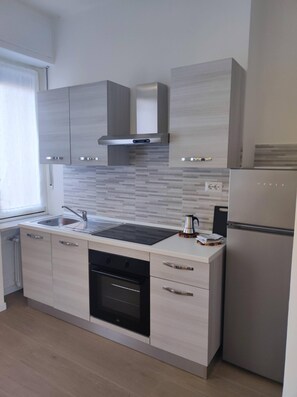 Een koelkast, een oven, een kookplaat, kookgerei, borden en bestek