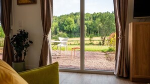 A room with a large window, a potted plant, a white chair, and a wooden cabinet. - Gîte Jardin: 50 m2 gîte for 2 to 4 people with terrace overlooking garden (Le Bô)