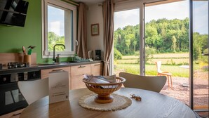 A modern kitchen with a dining area, large windows, and a view of a green landscape. - Gîte Jardin: 50 m2 gîte for 2 to 4 people with terrace overlooking garden (Le Bô)
