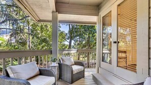 A covered porch with wicker furniture, a small table, and a door with blinds. - Fairway View Getaway in Palmetto Dunes (Hilton Head Island)