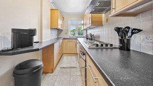 A modern kitchen with a black countertop, stainless steel appliances, and wooden cabinets. - *Modern Spacious studio flat in Ealing* (Hangerlane )