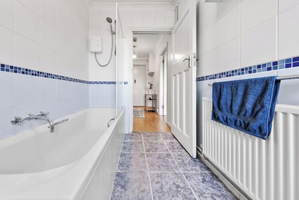 Een badkamer met een bad, witte betegelde wanden en een blauwe tegelvloer.