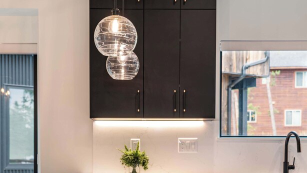 A modern kitchen with dark cabinets, a white marble island, pendant lighting, and a window with a view of buildings. - Walk to Town | Near Free Shuttle (Fraser)