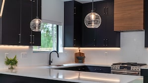 A modern kitchen with black cabinets, a white countertop, a large island with stools, and pendant lighting. - Walk to Town | Near Free Shuttle (Fraser)