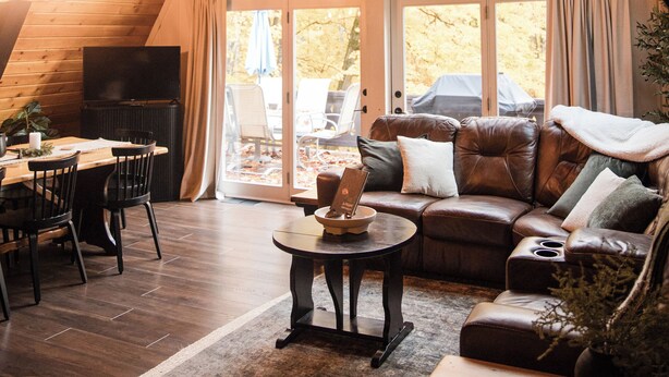 Una habitación estilo loft acogedora, con techo de madera, un ventanal grande, un sofá de cuero y un comedor.