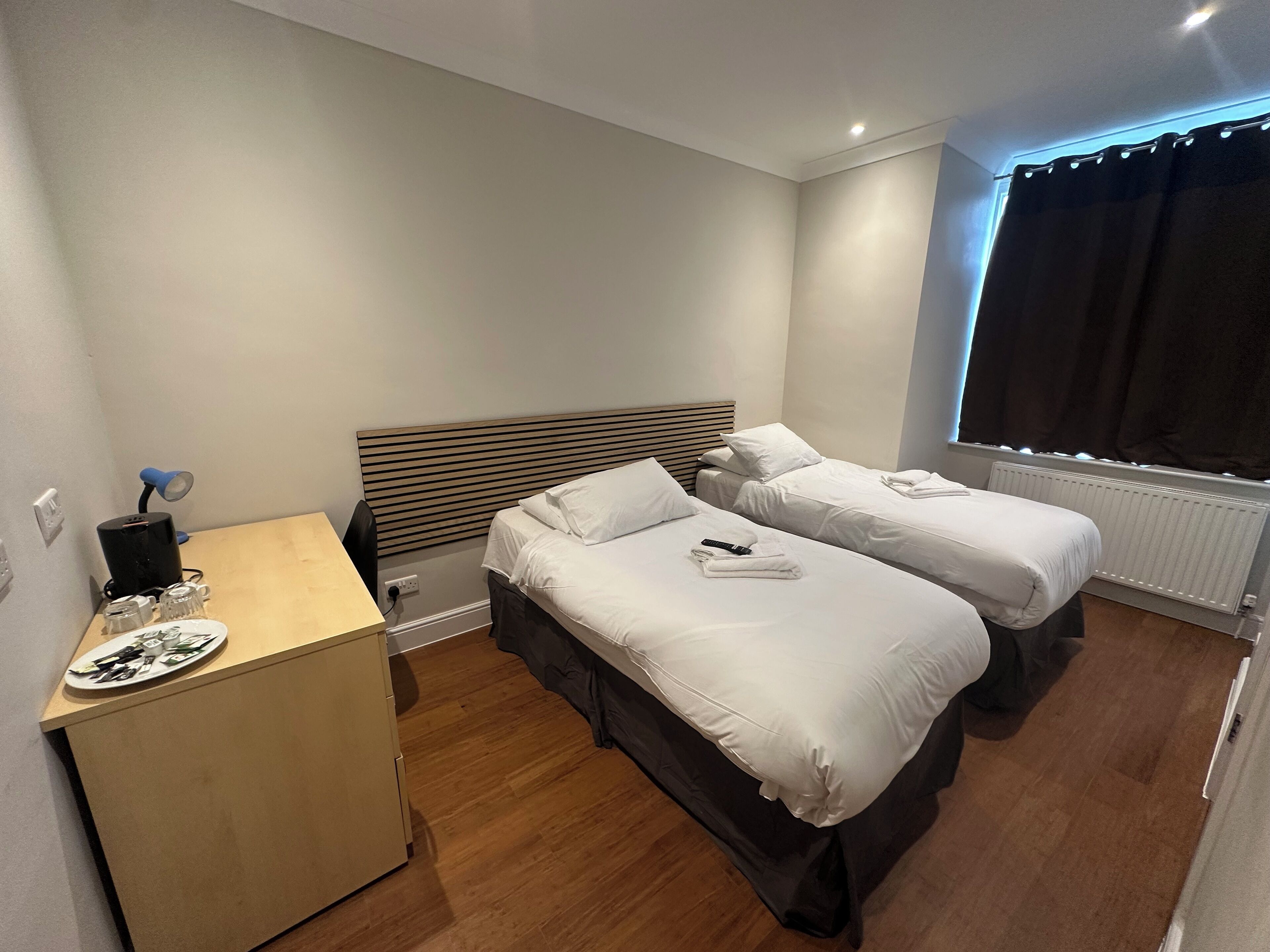 A hotel room with two beds, a desk, and a window with curtains.