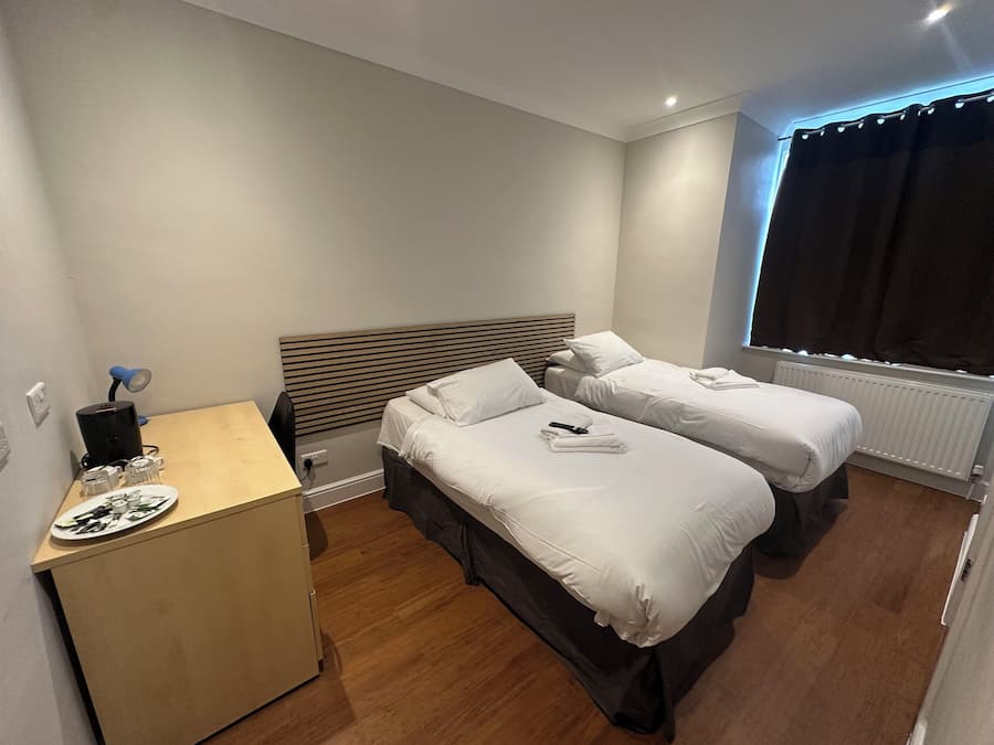 A hotel room with two beds, a desk, and a window with curtains.