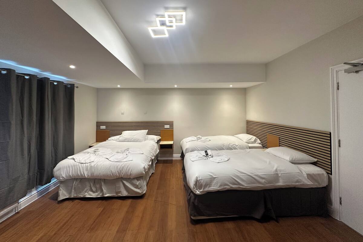 A hotel room with two beds, a wooden floor, and a modern ceiling light fixture.