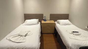 A hotel room with two single beds, a wooden nightstand with drawers, a desk, and a small table.