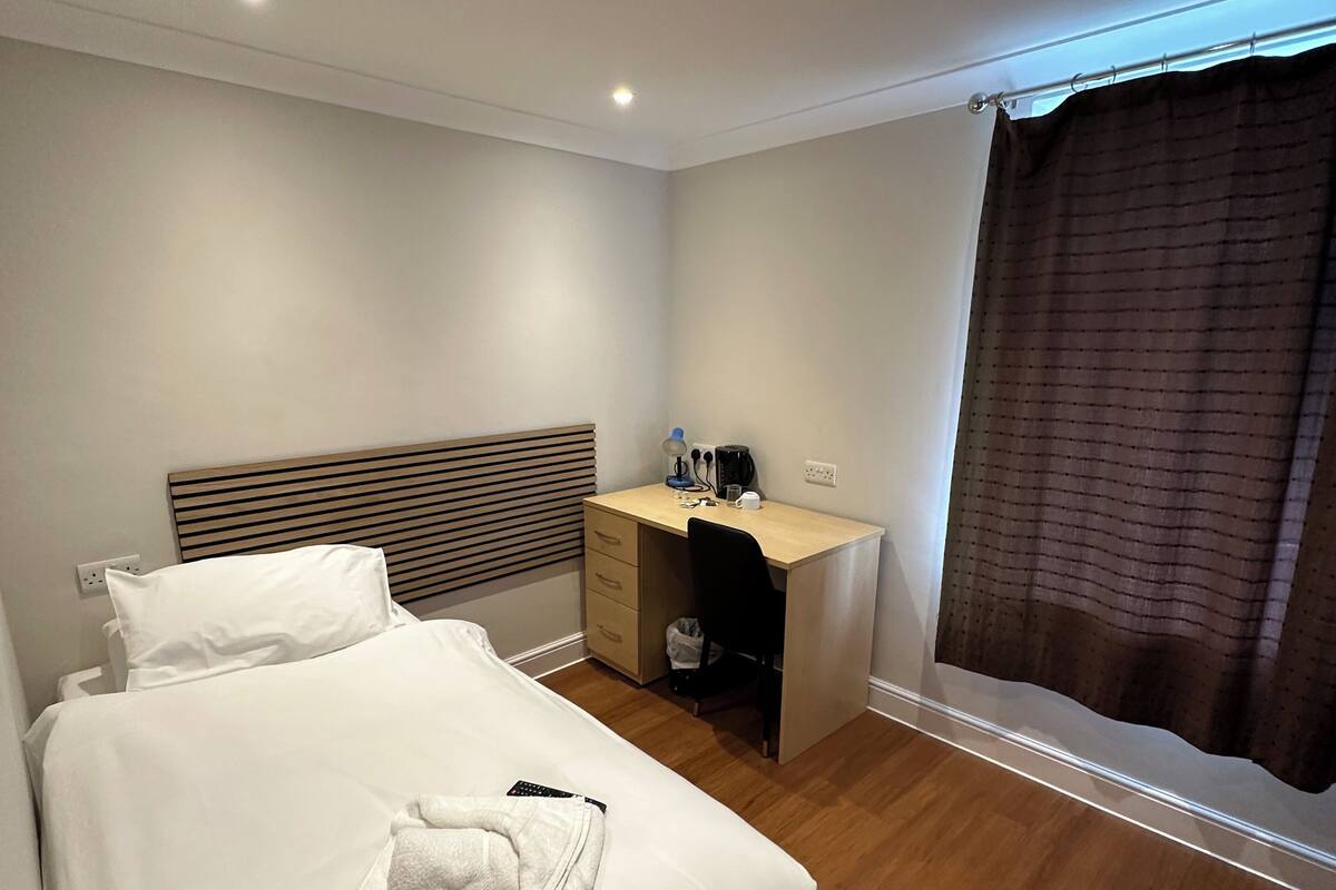 A hotel room with a bed, a desk, and a window with curtains.
