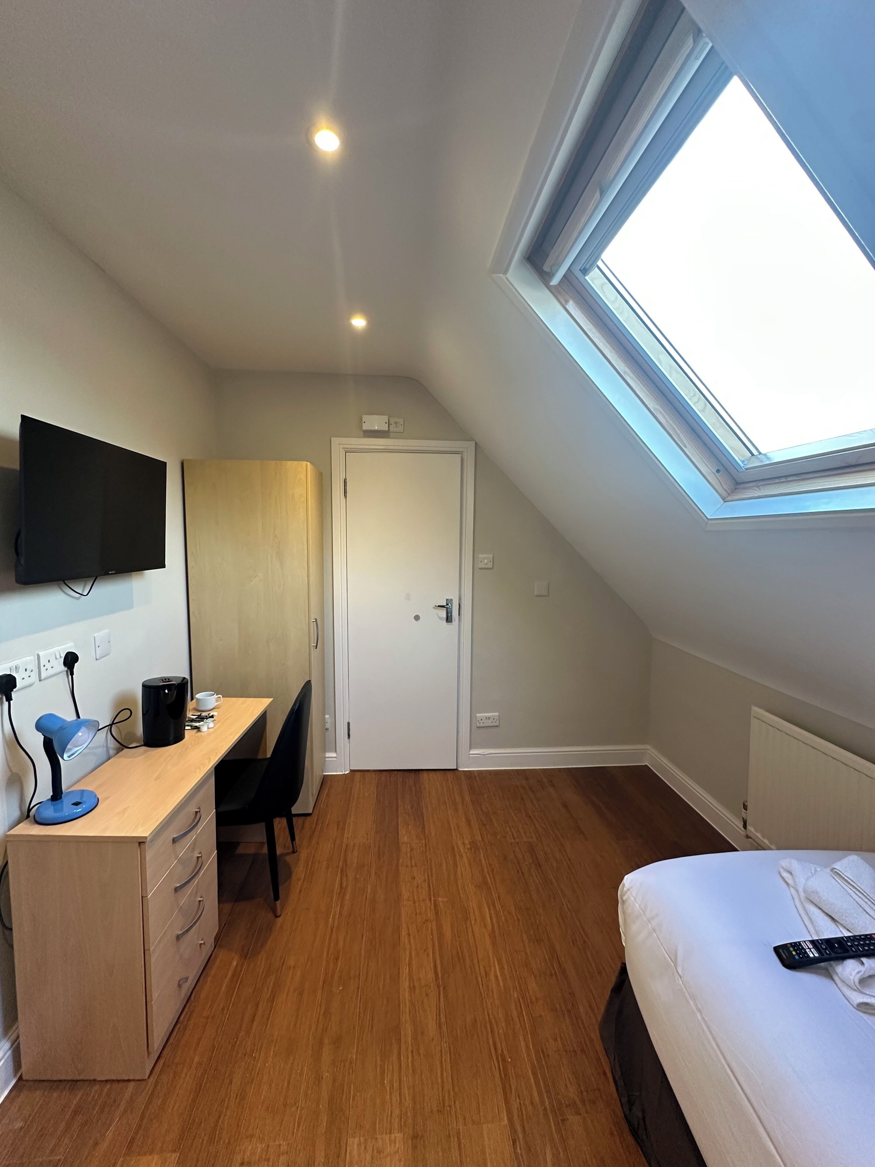 A bedroom with a skylight, a bed, a desk with a chair, and a television.