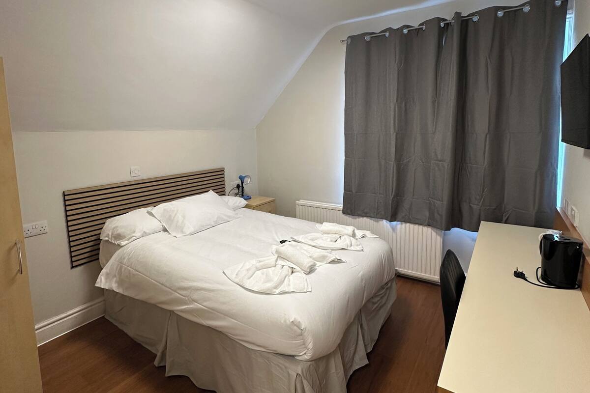 A bedroom with a bed, bedside tables, a desk, and a window with curtains.