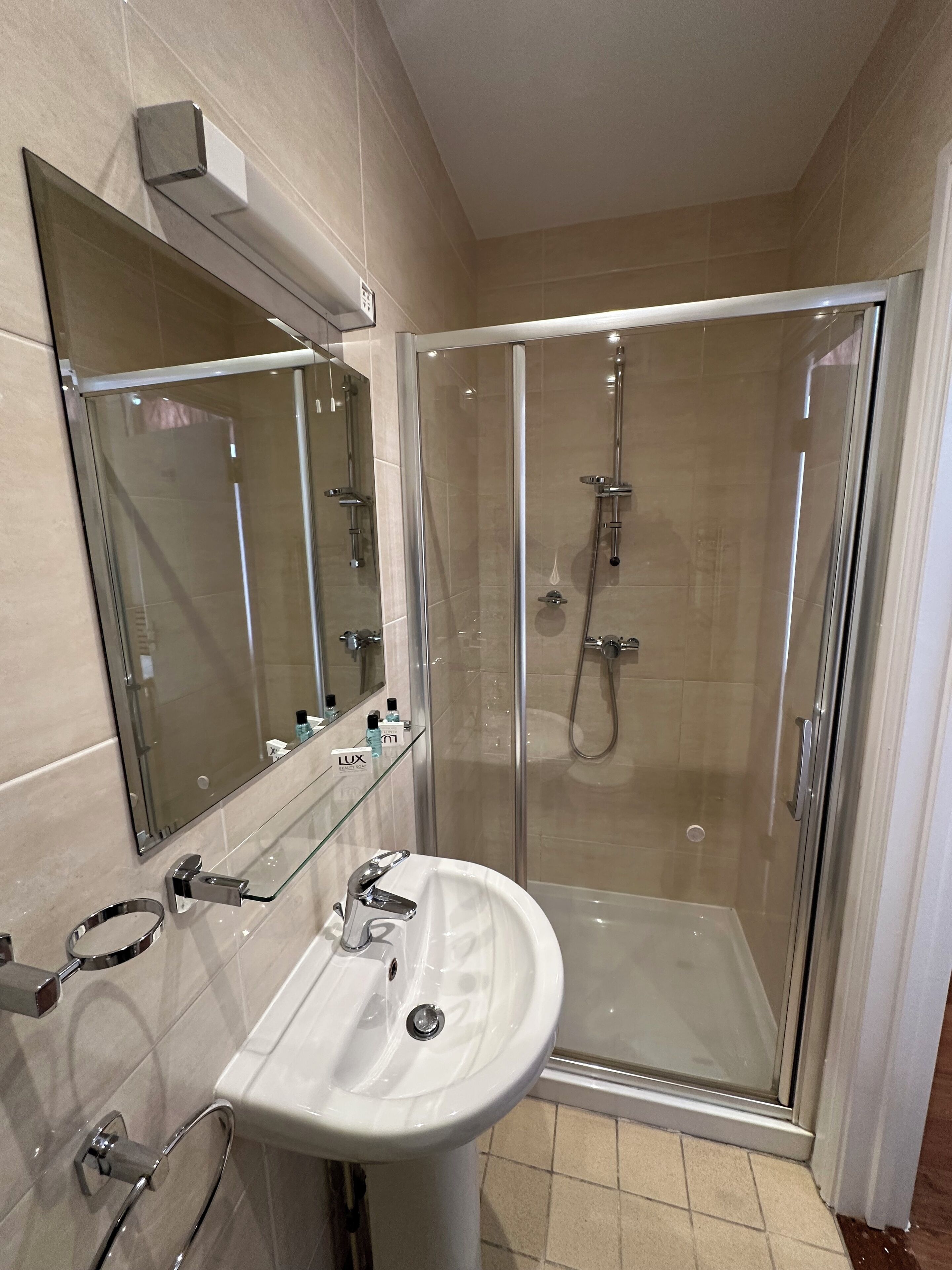 Ein modernes Badezimmer mit einer gläsernen Duschkabine, einem weißen Waschbecken und einem großen Spiegel.